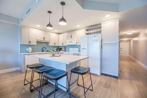 Una cocina moderna con armarios blancos, una isla central con taburetes y un microondas integrado.