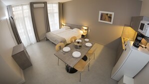 Habitación de hotel con cama, mesitas de noche, una mesa de comedor para dos personas, microondas y una pequeña kitchenette.