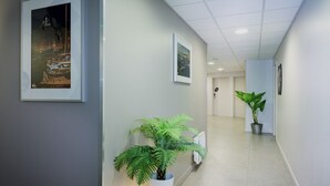 Un pasillo con obras enmarcadas en las paredes, plantas en macetas y una puerta al final.