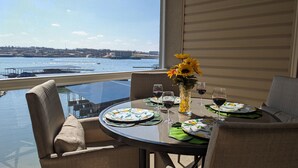 Mesa de jantar com cadeiras, vaso com girassóis e copos de vinho em varanda com vista para o cais.