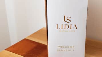 A white paper bag with gold lettering reading "IS LIDIA ROOMS & SUITES" and "WELCOME BENVENUTI" on a wooden surface.
