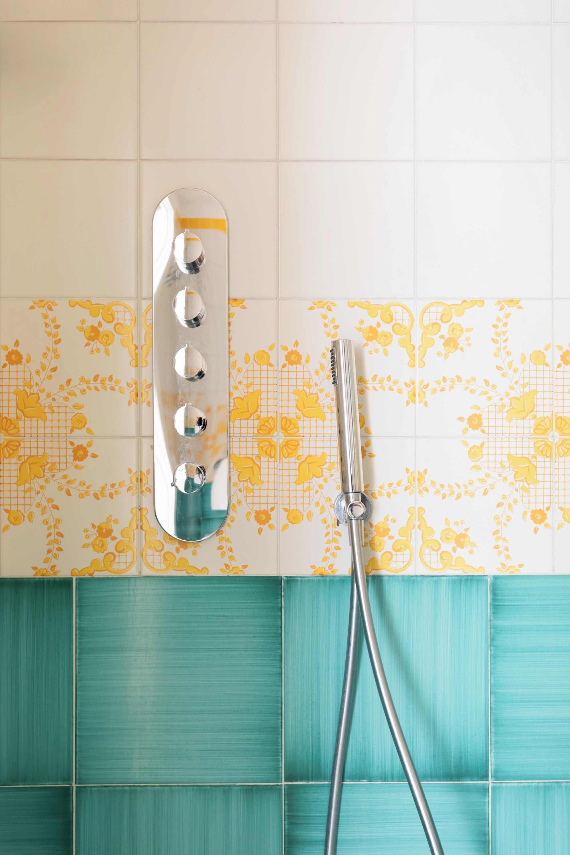 A bathroom with a showerhead mounted on a tiled wall, featuring a floral pattern and a teal accent wall.