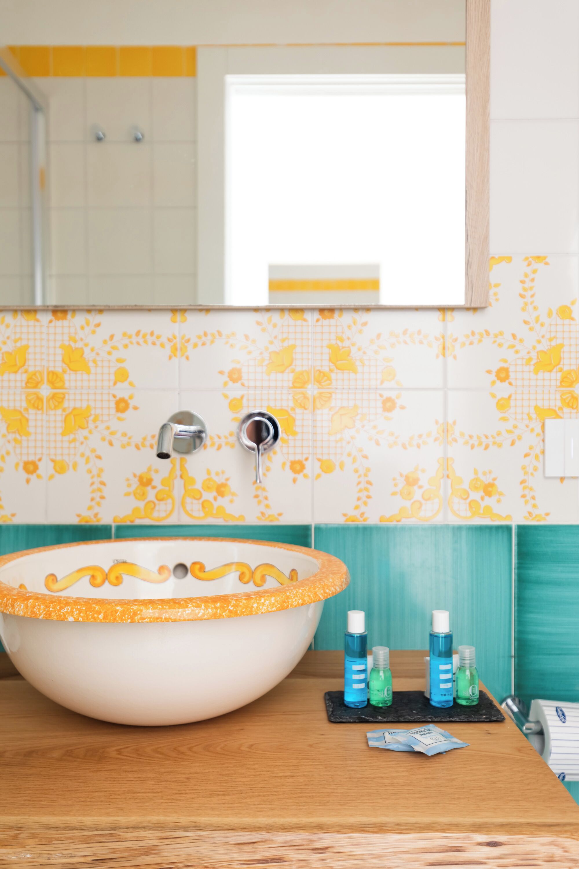 A bathroom with a large oval sink, a mirror, and a tiled backsplash with floral patterns.
