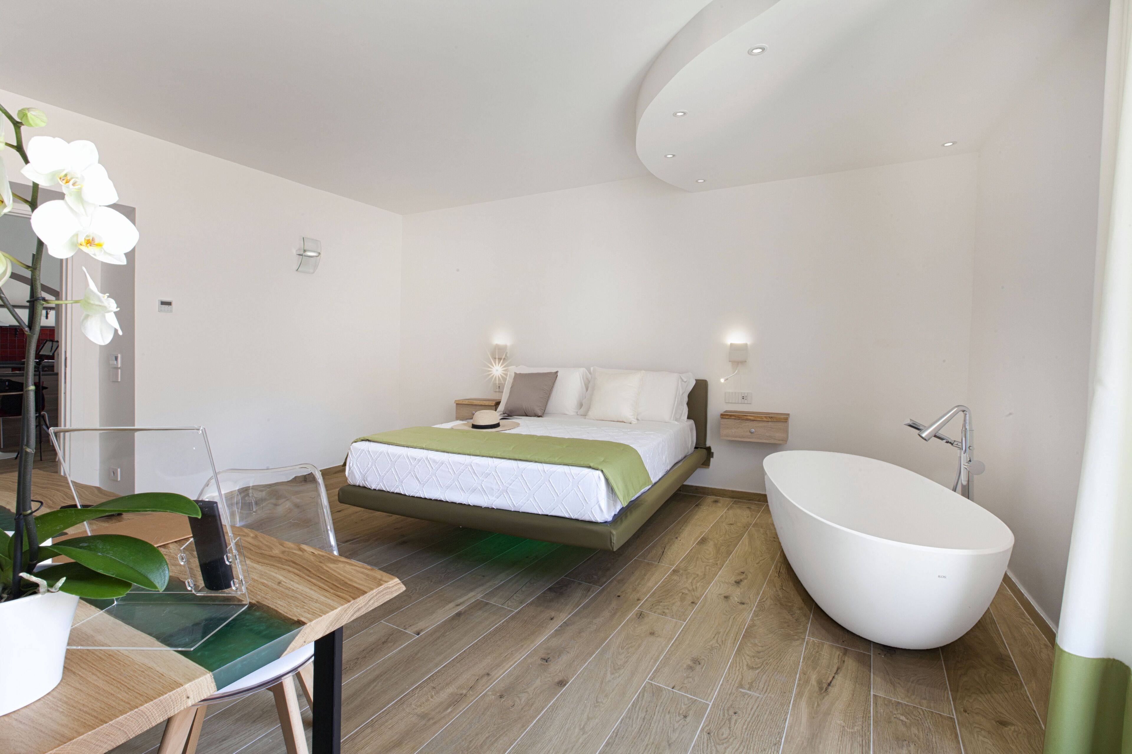 A modern bedroom with a large bed, a freestanding bathtub, and a wooden floor.