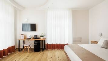 Une chambre d’hôtel avec un bureau en bois, un lit, un téléviseur fixé au mur et une fenêtre avec des rideaux.