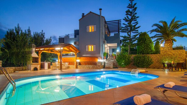 Una piscina con lettini da sole e un'area salotto coperta, circondata da un muro in pietra e alberi.