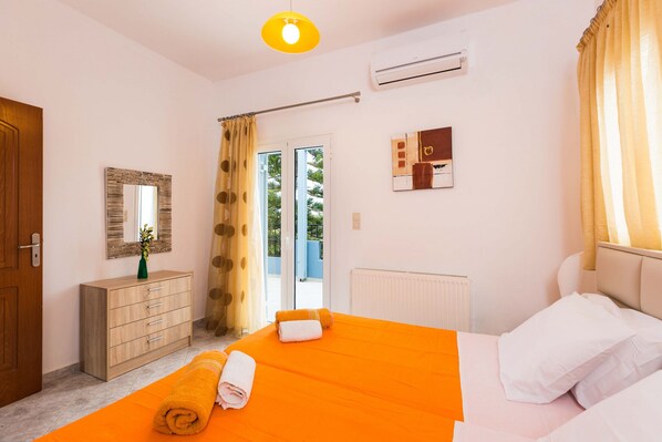 A hotel room with a bed, a wooden dresser, a mirror, an air conditioning unit, and a view through the glass door. - Blue Villa 2 - With Private Pool (Perama)