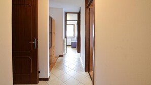A hallway with wooden doors and tiled flooring, leading to a room with a window and a radiator.