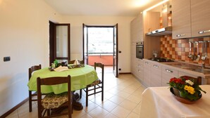 A compact kitchen with a dining area, featuring a green tablecloth, wooden chairs, and a view through an open door.