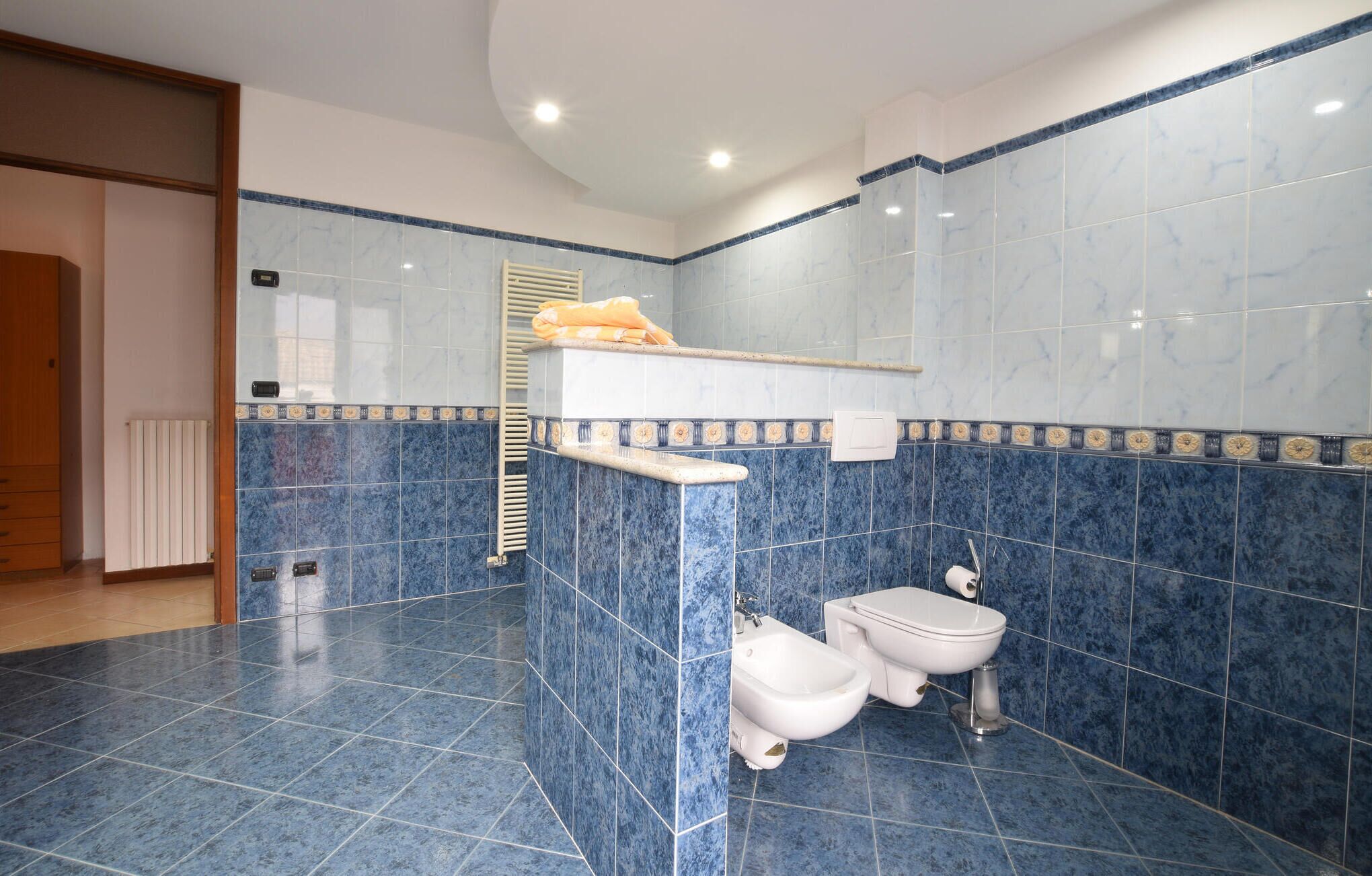 A bathroom with blue marble tiles, a toilet, bidet, and a towel rack.