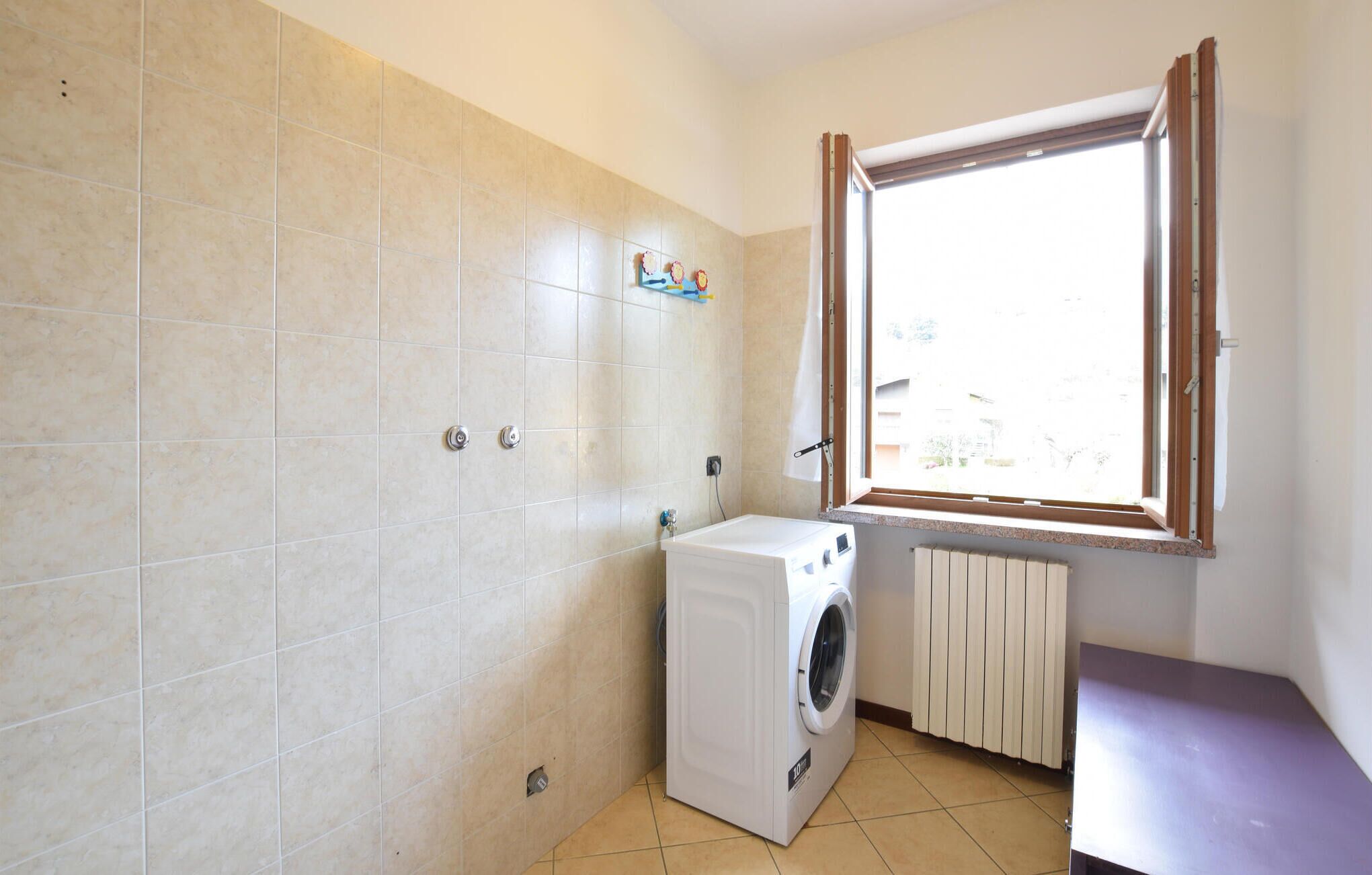 A laundry room with a washing machine, a radiator, and a window with curtains.