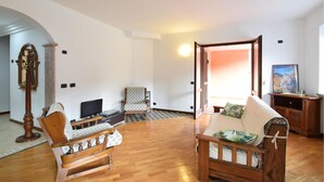 A spacious living room with a wooden floor, a sofa, a chair, a television, and a painting on the wall.
