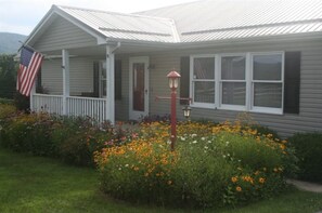 A house with a porch, an American flag, and a garden with flowers.