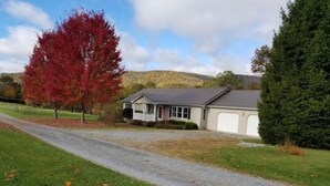 A single-story house with a garage, a gravel driveway, and a red-leaved tree in the foreground. - Drennen Ridge Farm Guest House (Marlinton)