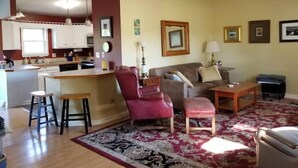 A living room with a sofa, armchair, and ottoman, a kitchen area with a bar, and a ceiling fan. - Drennen Ridge Farm Guest House (Marlinton)