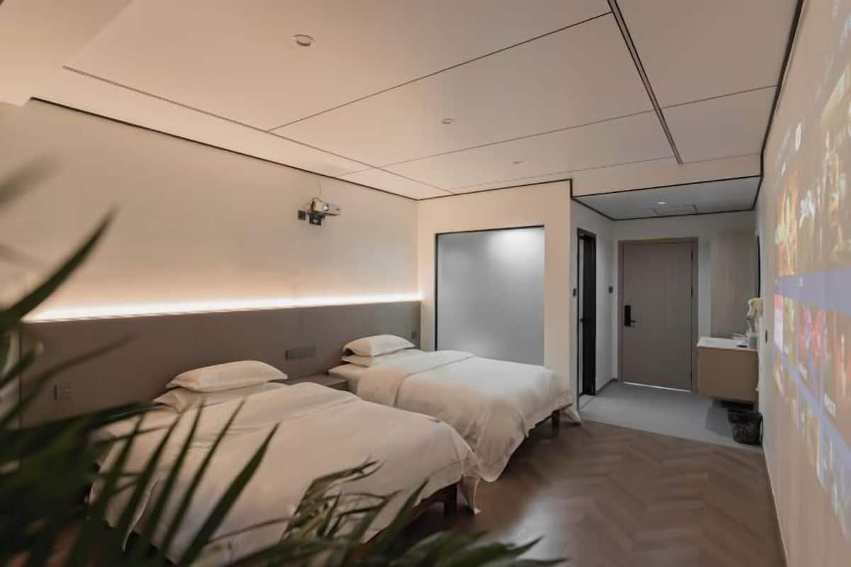 Een moderne hotelkamer met twee bedden, een wandprojector en een klein bureau.