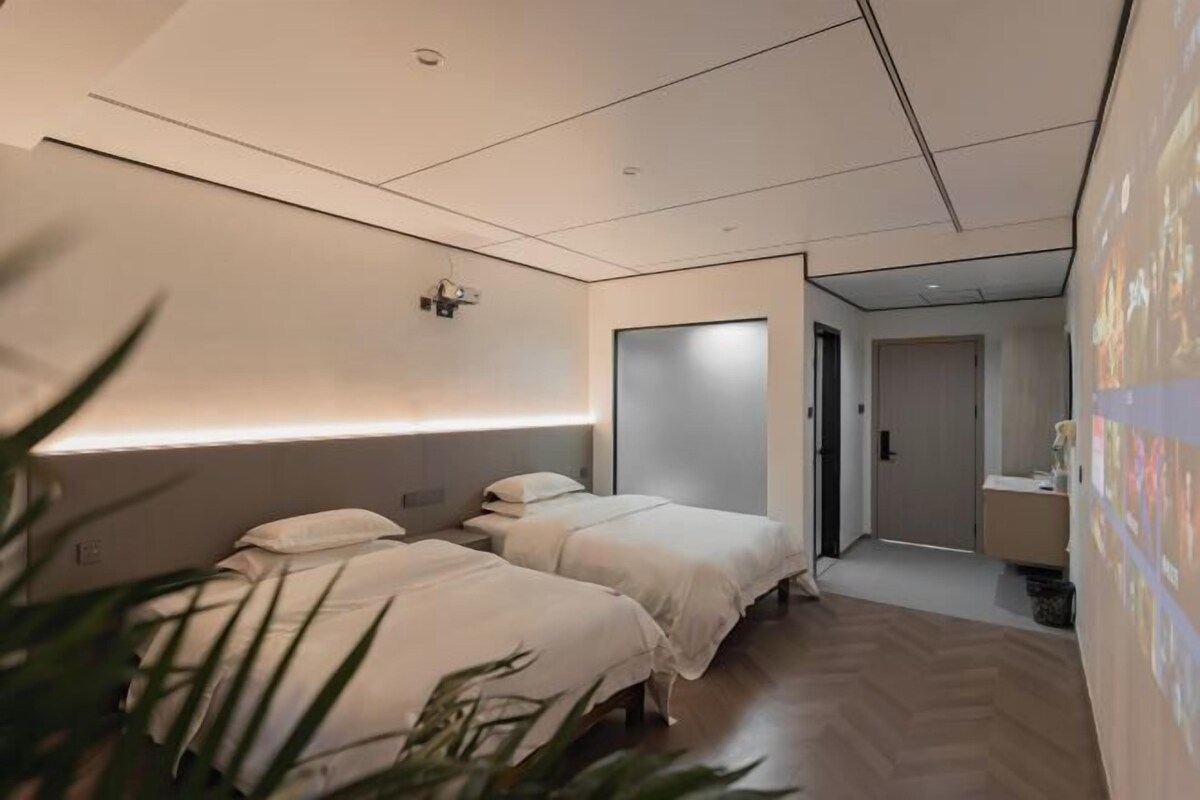 Une chambre d’hôtel moderne équipée de deux lits, d’un projecteur fixé au mur et d’un petit espace bureau.