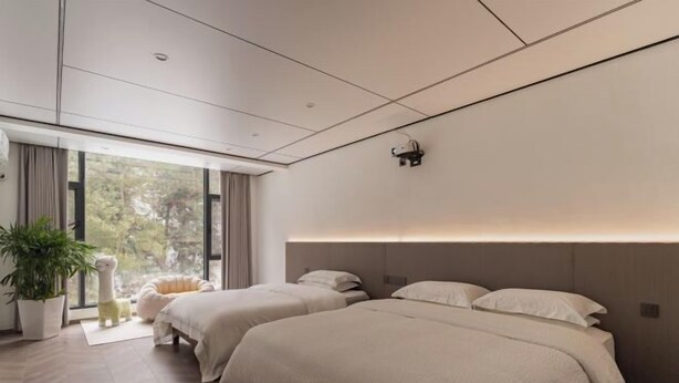 Une chambre d’hôtel moderne avec deux lits, une grande fenêtre, une plante en pot et un fauteuil confortable.