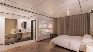 Une chambre d’hôtel moderne dotée d’un grand lit, d’une coiffeuse avec un miroir, d’une étagère contenant des articles de toilette et d’un écran de projection mural diffusant des images.