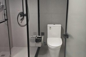 Ein kleines, geschlossenes Badezimmer mit Toilette, Mülleimer und Duschbereich.