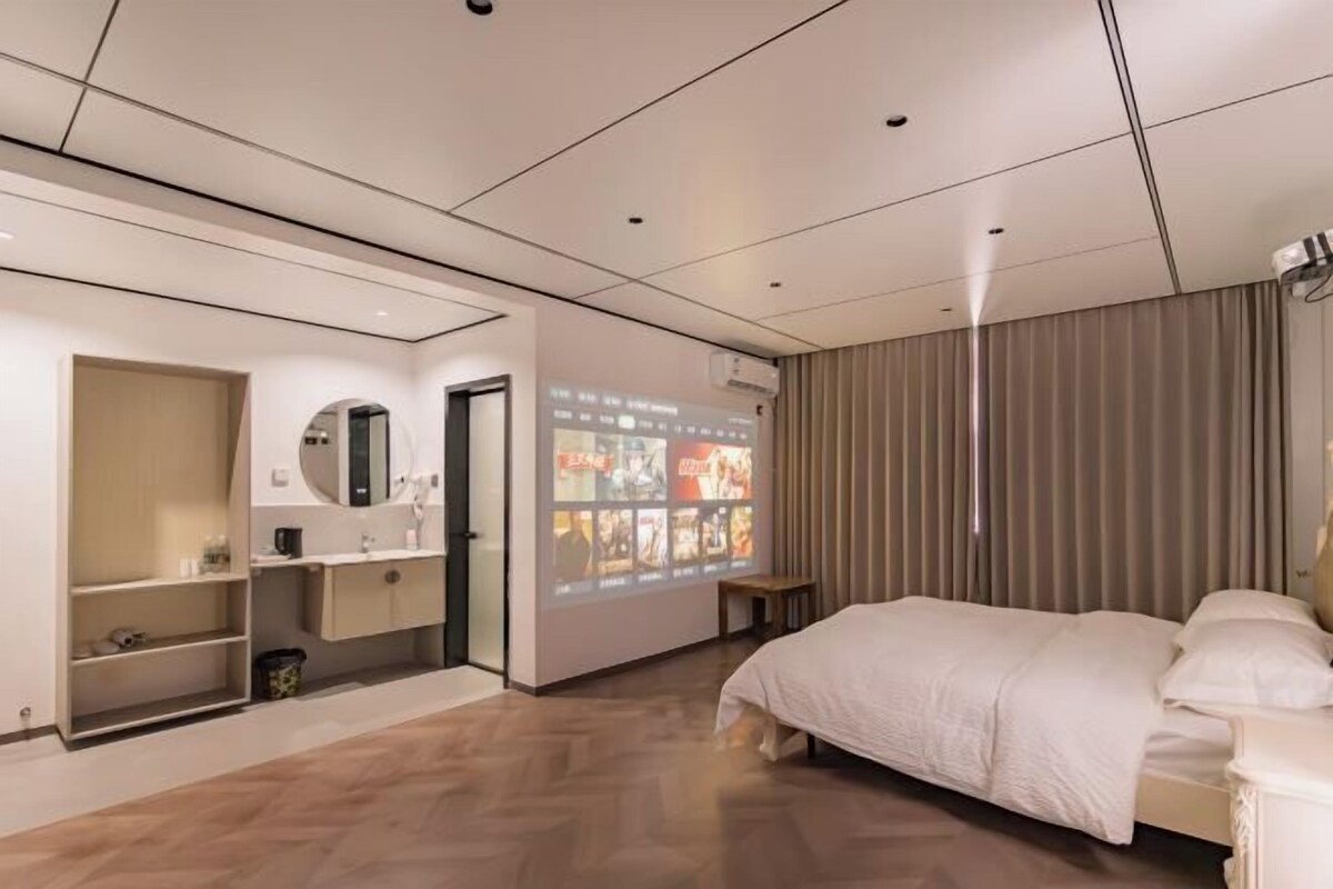 Une chambre d’hôtel comprenant un lit, une coiffeuse avec un miroir, une étagère avec des articles de toilette, un écran de projection et un rideau.
