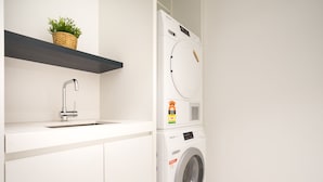 Une buanderie moderne équipée d’un lave-linge, d’un évier et d’une étagère sur laquelle est posée une plante.