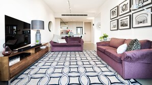 Un salon moderne avec un téléviseur à écran plat, une console, deux canapés, un tapis à motifs et un coin repas à l’arrière-plan.