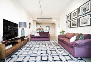 Un soggiorno moderno con una TV a schermo piatto, un tavolo consolle, due divani, un tappeto decorato e, sullo sfondo, un'area pranzo.