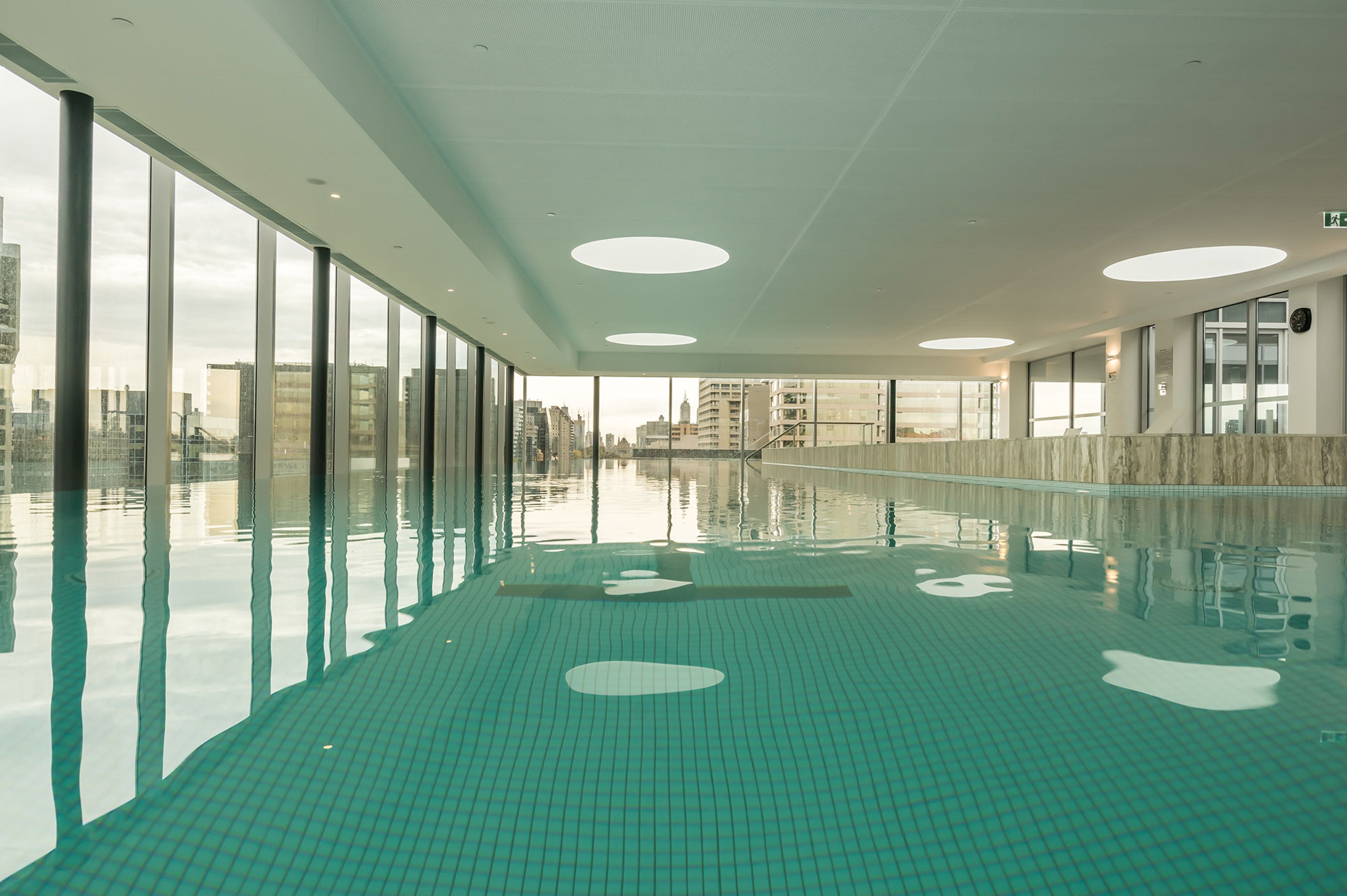 A swimming pool with a tiled floor and large windows on one side.