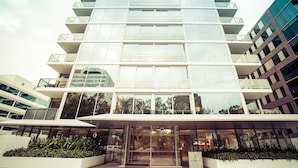 En modern byggnad med flera våningar, en fasad av glas, en central entré och ett anlagt område med växter.