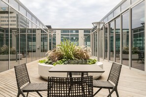 A modern outdoor seating area with a central planter, surrounded by glass walls and a wooden deck. - The Fawkner Stylish Saint Kilda Apartment (Melbourne)
