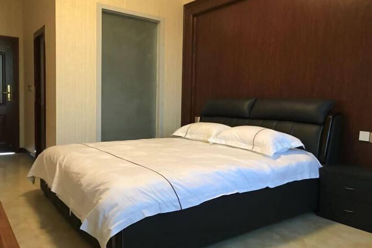 A bedroom with a large bed, a wooden headboard, and a dark-colored nightstand.