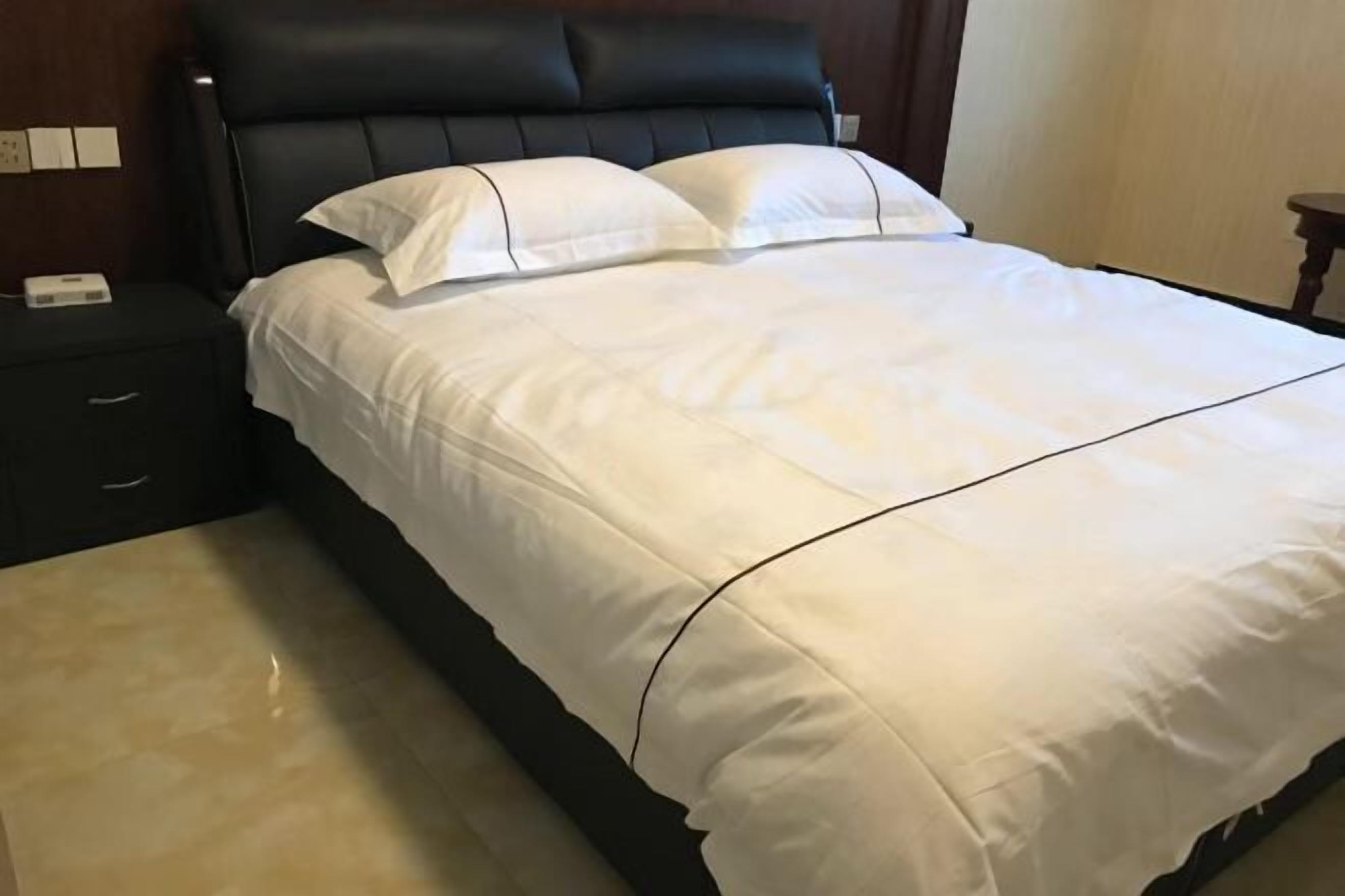 A bed with white bedding, a black headboard, and a wooden nightstand with a lamp.