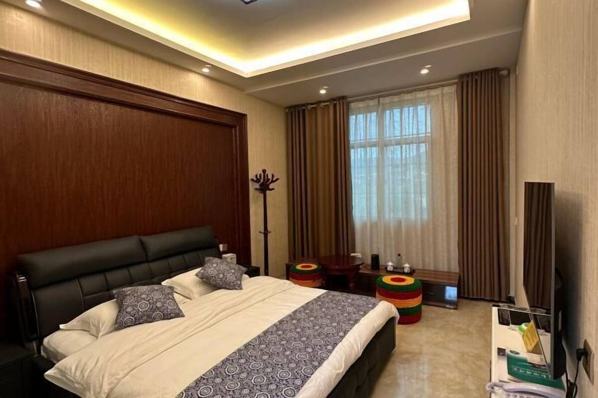 A modern hotel room with a large bed, a flat-screen TV, a desk, and a window with curtains.