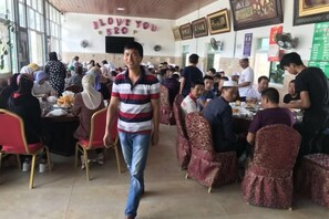 Un comedor interior con mesas y sillas, una persona caminando y una pared con un mensaje.