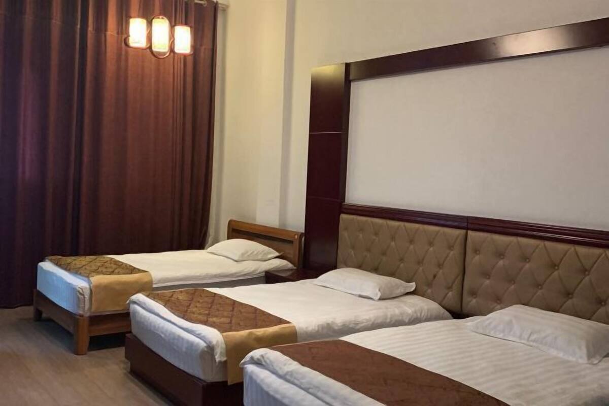 A hotel room with two single beds, a large headboard, and a curtain.