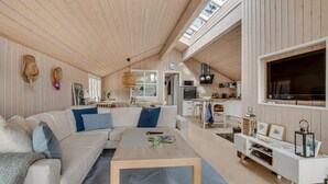 Tilava olohuone, jossa on suuri sohva, sohvapöytä ja seinälle asennettu televisio.