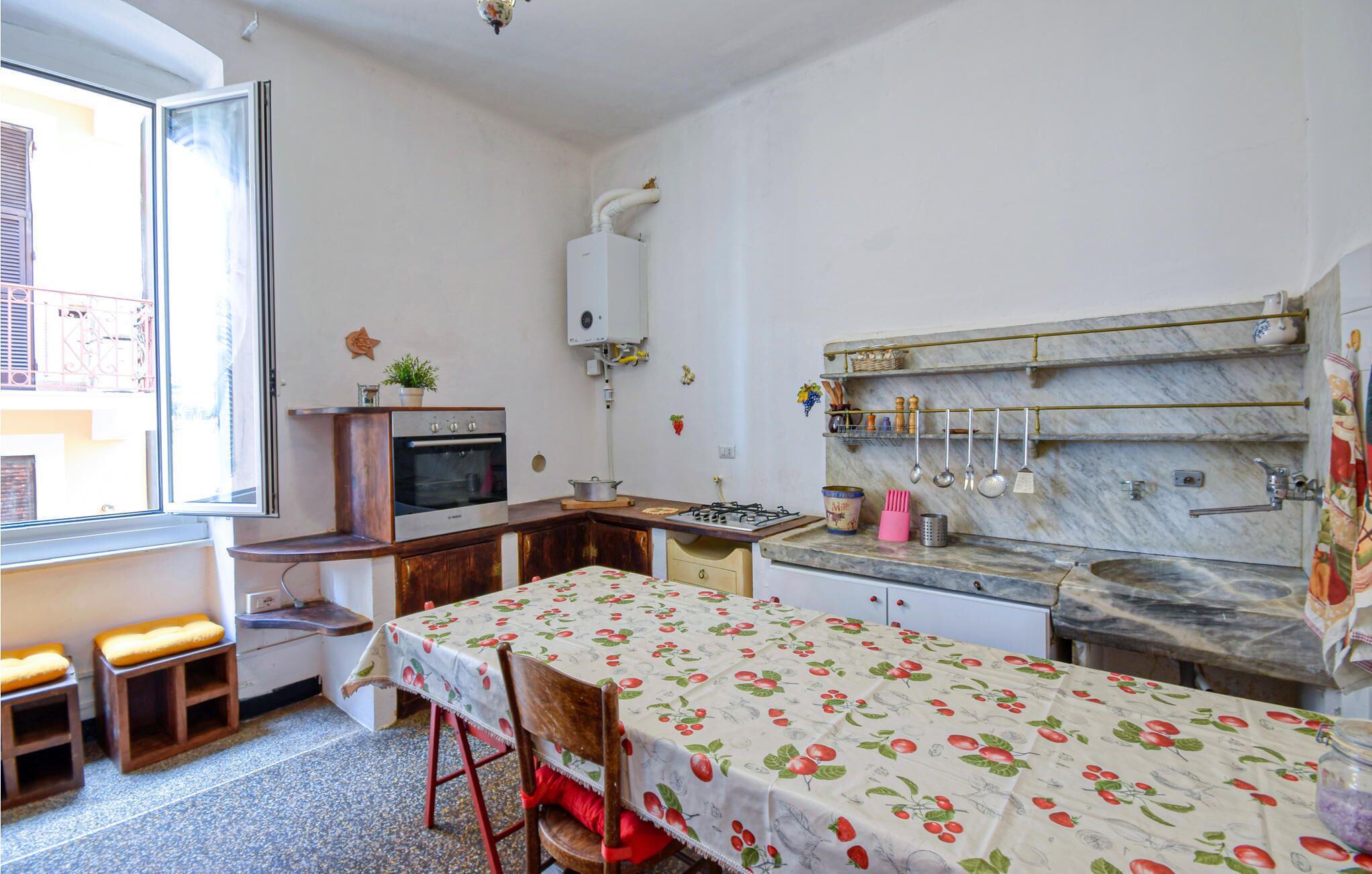 A compact kitchen with a gas stove, oven, and marble countertop. There is a dining table with a floral tablecloth and a chair.