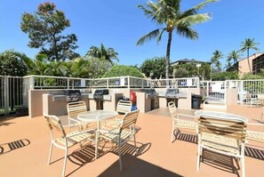 Relax in a serene outdoor space surrounded by lush greenery and tropical plants, complete with a seating area and barbecue grills.