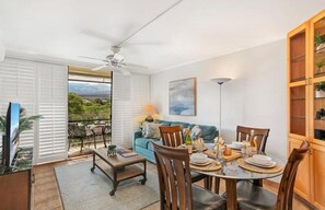 Enjoy a spacious living area with a dining table and comfortable seating, leading to a balcony with a scenic view.