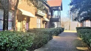 Ein schmaler Weg, der von Hecken gesäumt wird und zu einem Gebäude mit Backsteinfassade und einem kleinen Balkon führt.