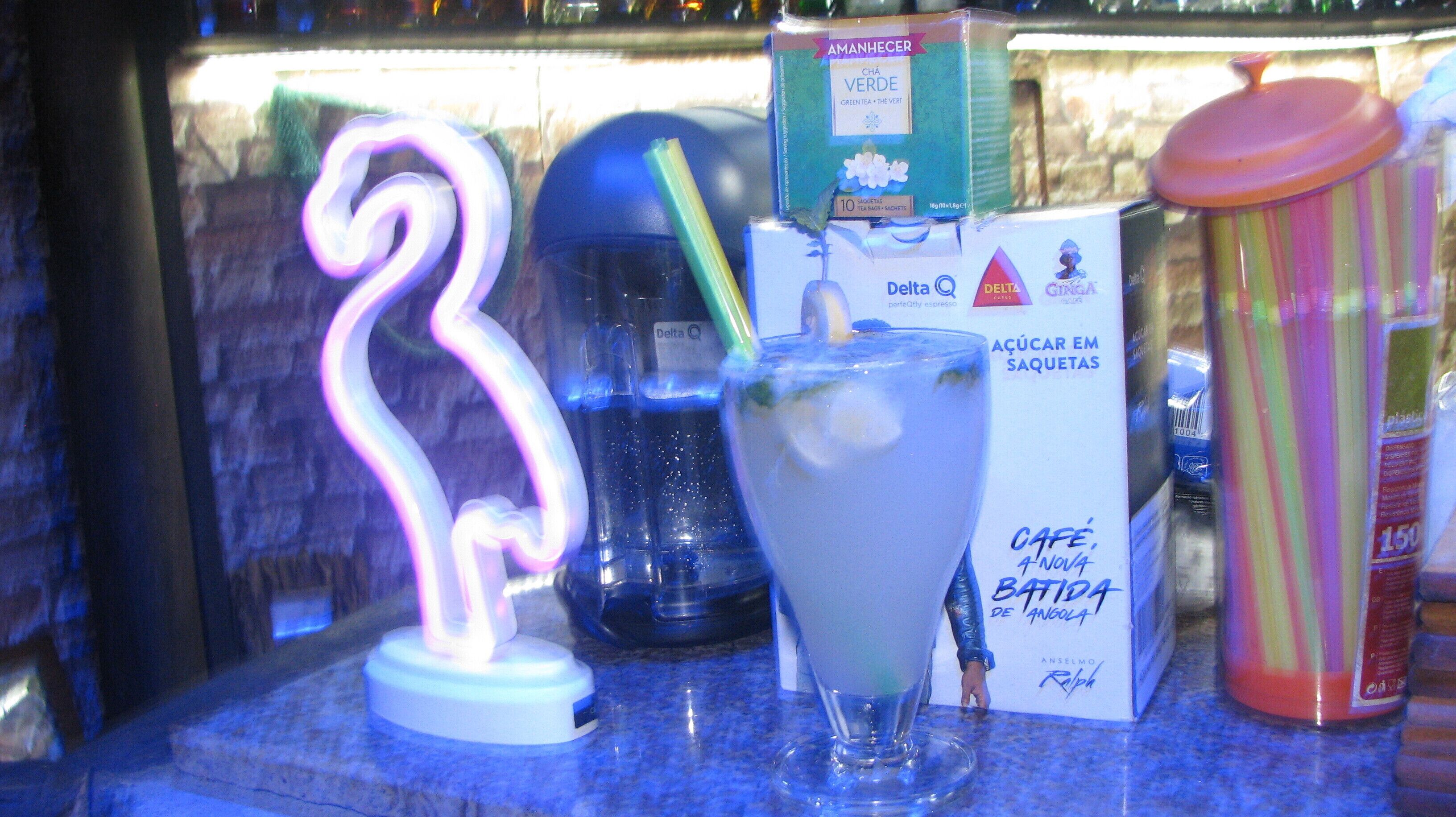 Een bar met een neonbord, een glas ijsthee en diverse objecten, waaronder een doos en een kleurrijke houder.