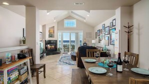 A spacious living area with a fireplace, dining table set for two, and a view through a large window.