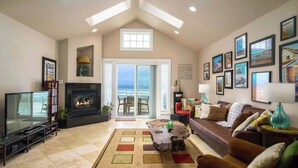 A living room with a fireplace, television, and a view of the ocean through large glass doors.