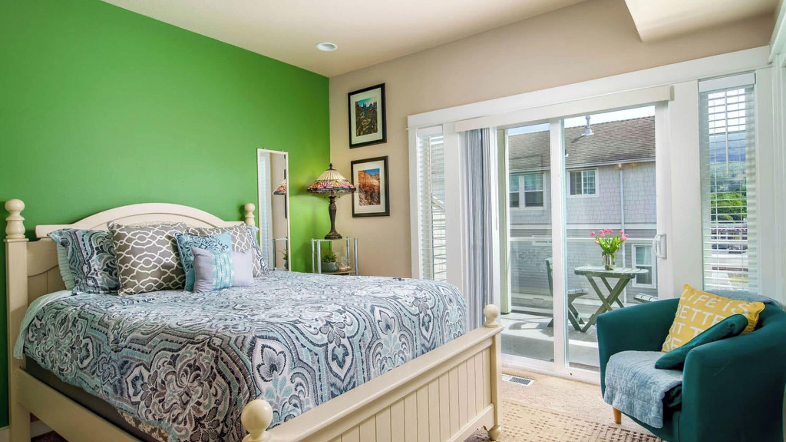A bedroom with a bed, a nightstand, a lamp, a chair, and a balcony with a view.