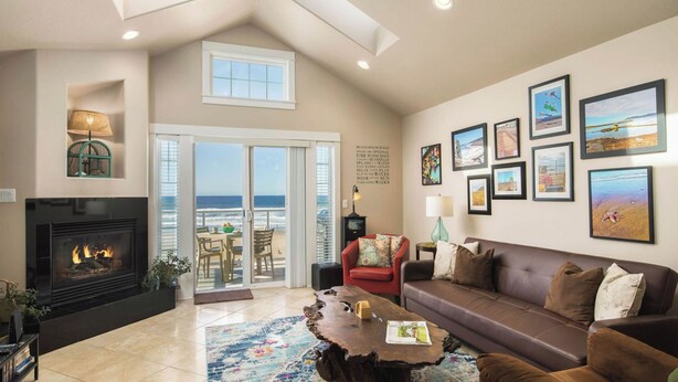 A living room with a fireplace, a sofa, a coffee table, and a view of the ocean through a sliding glass door.
