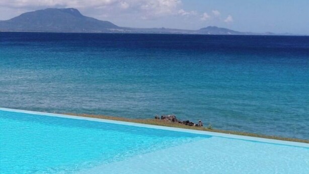 Une piscine à l’eau d’un bleu cristallin, une plage de sable et une montagne en arrière-plan.