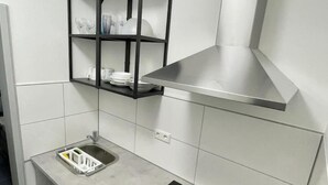 Une cuisine moderne dotée d’une hotte en acier inoxydable, d’un four encastré et d’une étagère noire placée au-dessus du plan de travail.