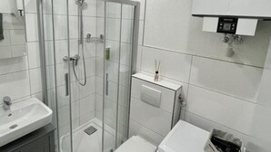Une salle de bain moderne avec une douche à parois de verre, un lavabo, des toilettes et un lave-linge.
