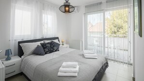 Une chambre à coucher avec un lit, des tables de chevet, une lampe, un radiateur et une vue sur l’extérieur.